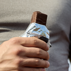 Man in a grey shirt holding a candy or protein bar with the wrapper pulled back
